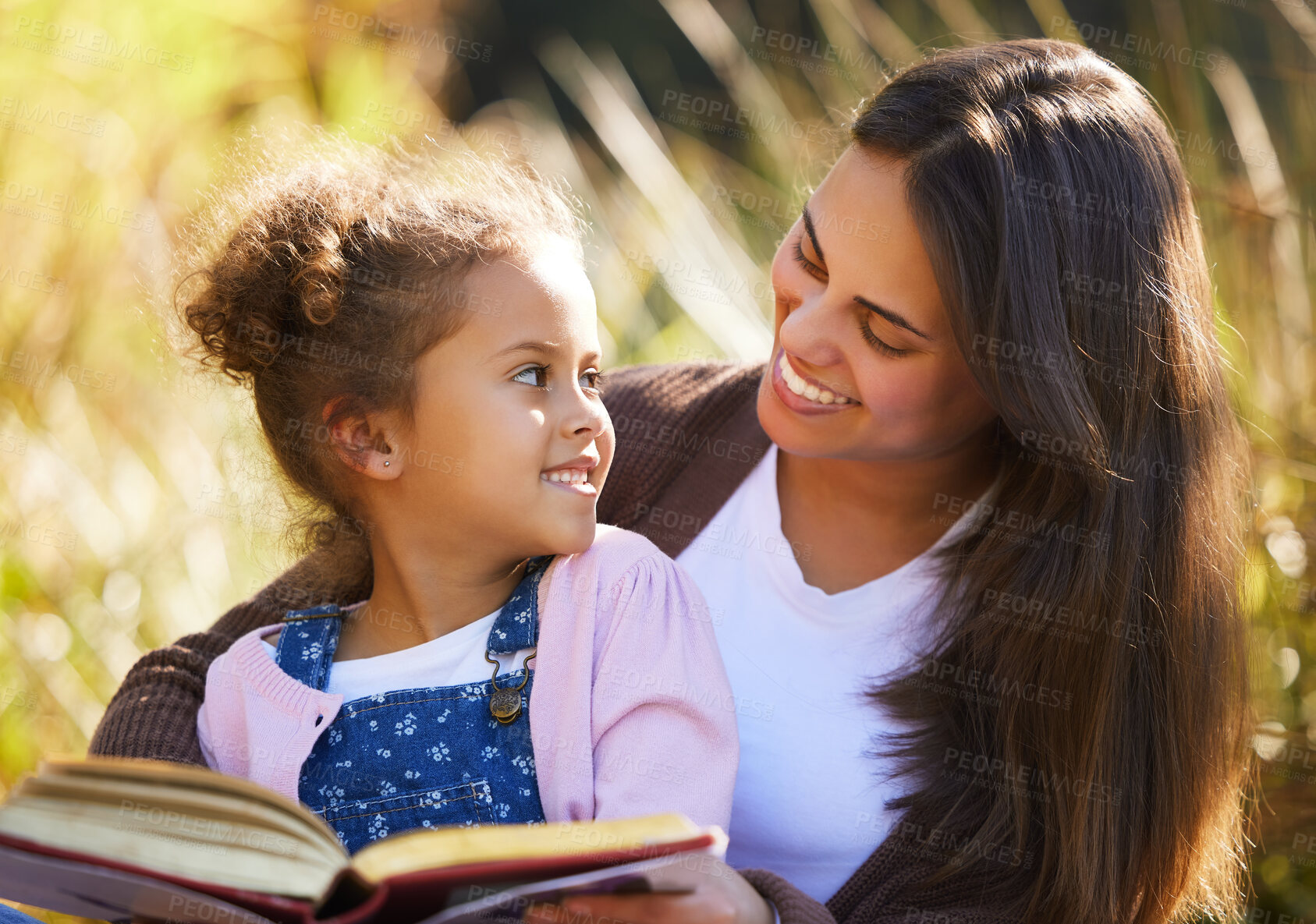 Buy stock photo Cropped shot of an attractive young woman reading to her daughter while picnicking in the park
