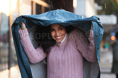 Buy stock photo Shot of a young woman covering herself with a coat in the rain in the city