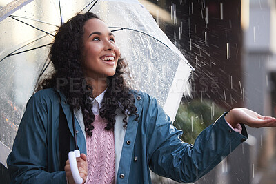Buy stock photo Shot of a young woman holding her hand out to feel the rain in the city