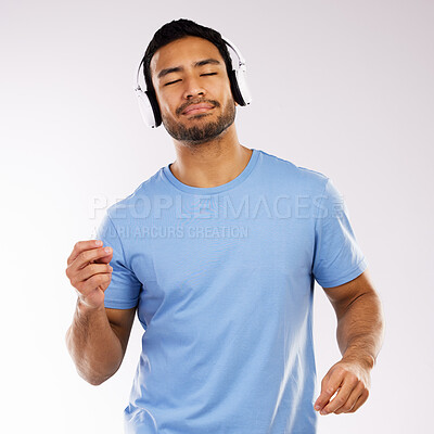 Buy stock photo Shot of a handsome man standing against a grey background in the studio and listening to music through headphones