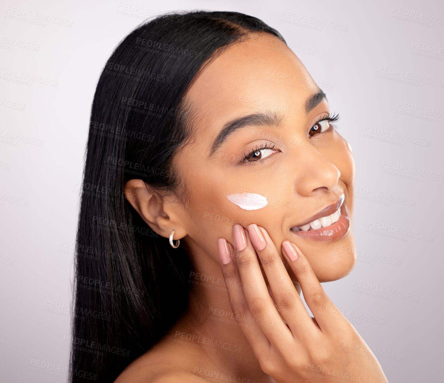 Buy stock photo Studio portrait of an attractive young woman applying moisturizer to her face against a pink background