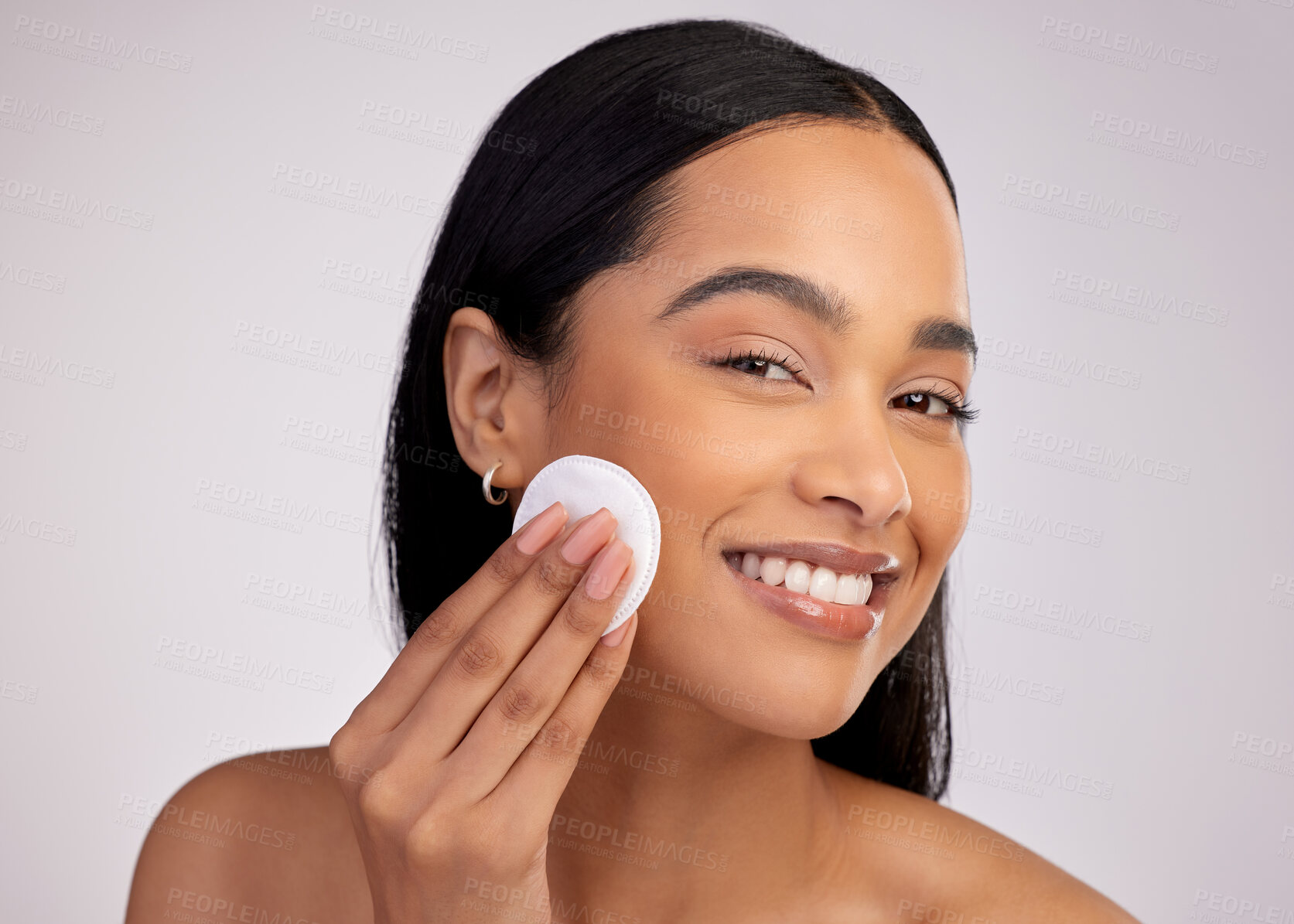 Buy stock photo Happy woman, cotton pad and cleaning face in skincare for makeup removal against a grey studio background. Portrait of female person wiping product, cosmetics or remove with swab for facial treatment