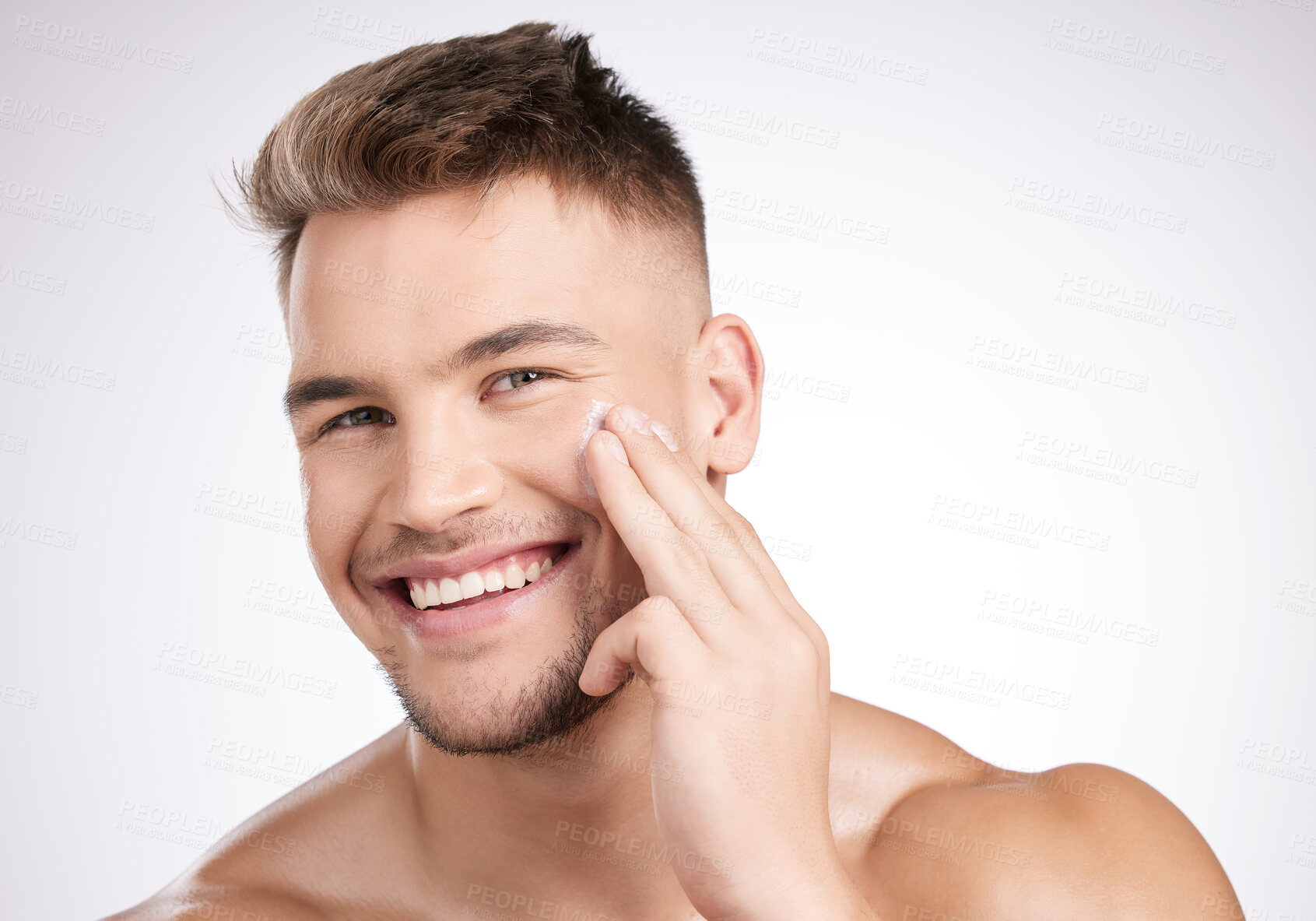 Buy stock photo Studio shot of a young man applying moisturizer to his face against a grey background