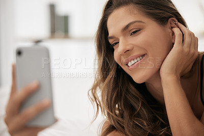 Buy stock photo Shot of a beautiful young woman using her cellphone while lying on her bed in lingerie at home