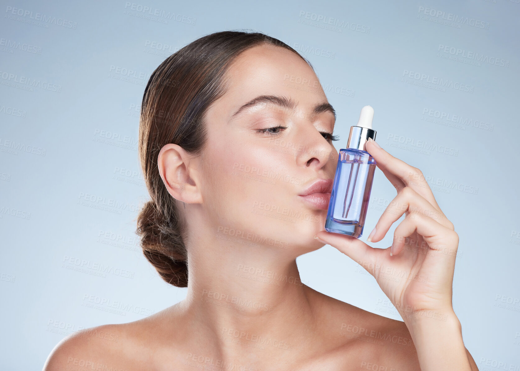 Buy stock photo Kiss, skincare and woman with beauty serum in studio, hand and product for glow and vitamin c. Dermatology, shine and bottle for aesthetic, hyaluronic acid and girl in blue background of spa for skin