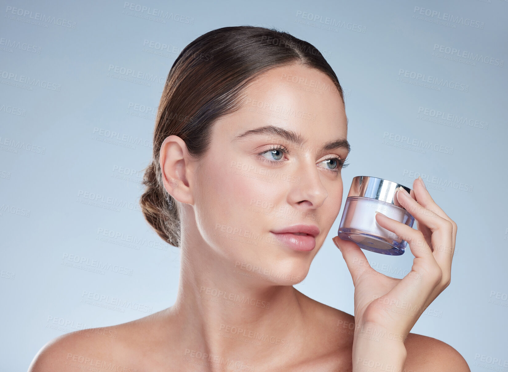 Buy stock photo Cropped shot of an attractive young woman posing with a container of moisturizer against a grey background