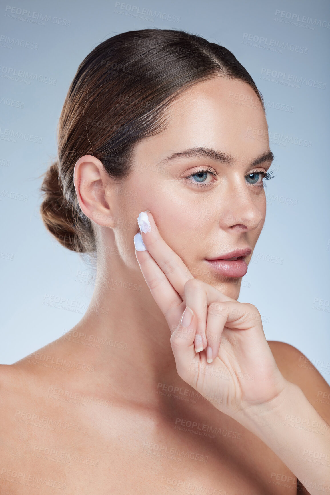 Buy stock photo Studio shot of an attractive young woman moisturizing her face against a grey background