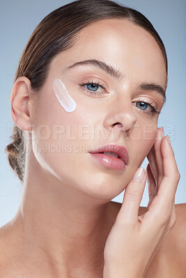 Buy stock photo Studio portrait of an attractive young woman moisturizing her face against a grey background