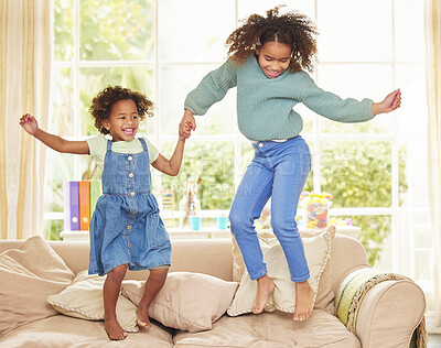 Buy stock photo Children, girls and holding hands for jumping in home, bonding and game for fun or love in childhood. Sisters, kids and playing together on couch in living room, happiness and weekend for support