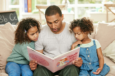 Buy stock photo Shot of a young father reading a book with his daughters at home