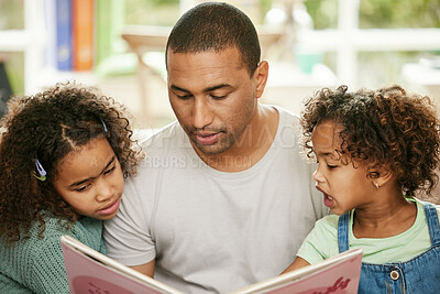 Buy stock photo Shot of a young father reading a book with his daughters at home