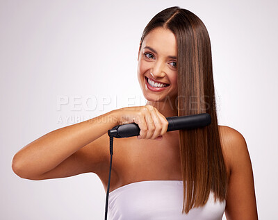 Buy stock photo Studio portrait of an attractive young woman straightening her hair against a grey background