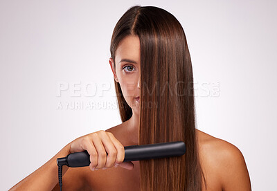 Buy stock photo Studio portrait of an attractive young woman straightening her hair against a grey background