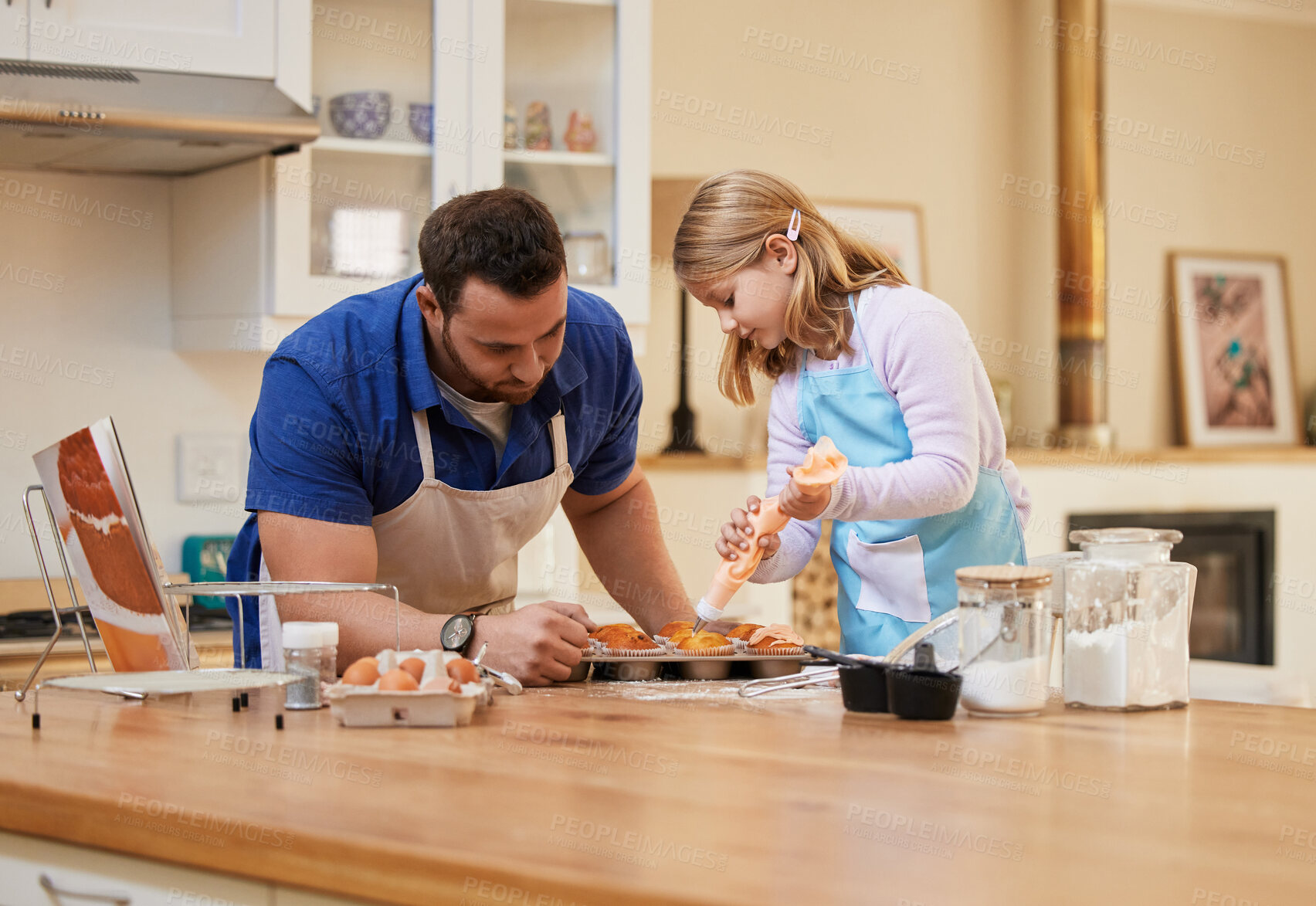 Buy stock photo Shot of a young man helping his daughter frost freshly baked cupcakes
