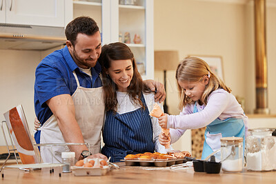 Buy stock photo Shot of a young mother and father watching as their daughter frosts cupcakes