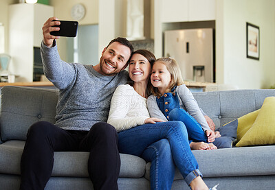 Buy stock photo Shot of a young family taking a selfie on the couch at home
