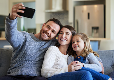 Buy stock photo Shot of a young family taking a selfie on the couch at home