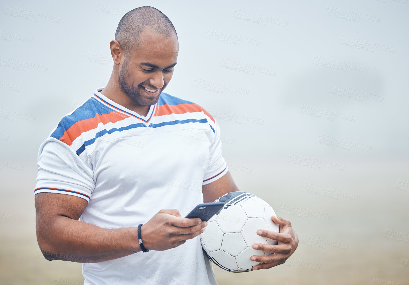 Buy stock photo Shot of a young male soccer player using his smartphone to send a text while holding the ball