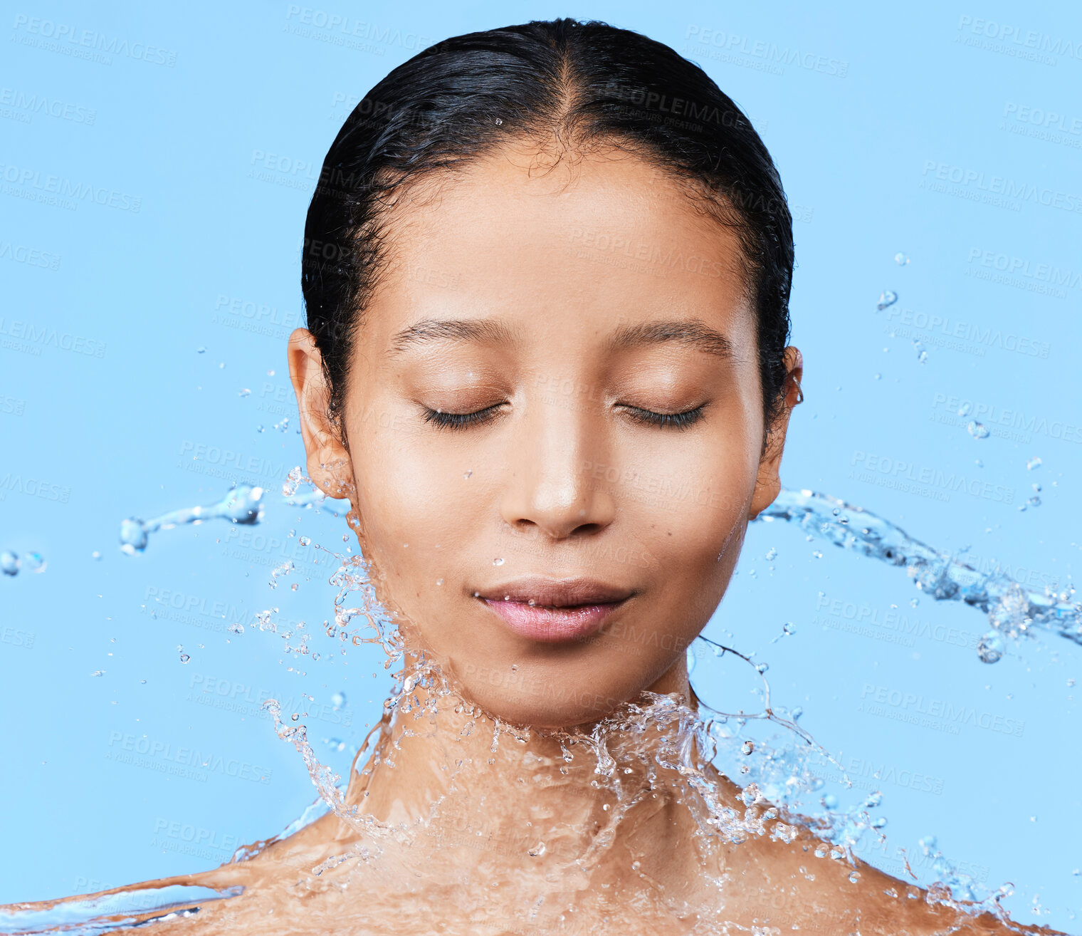 Buy stock photo Shot of a beautiful young woman being splashed with water against a blue background