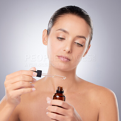 Buy stock photo Shot of a beautiful young woman applying serum to her face against a grey background