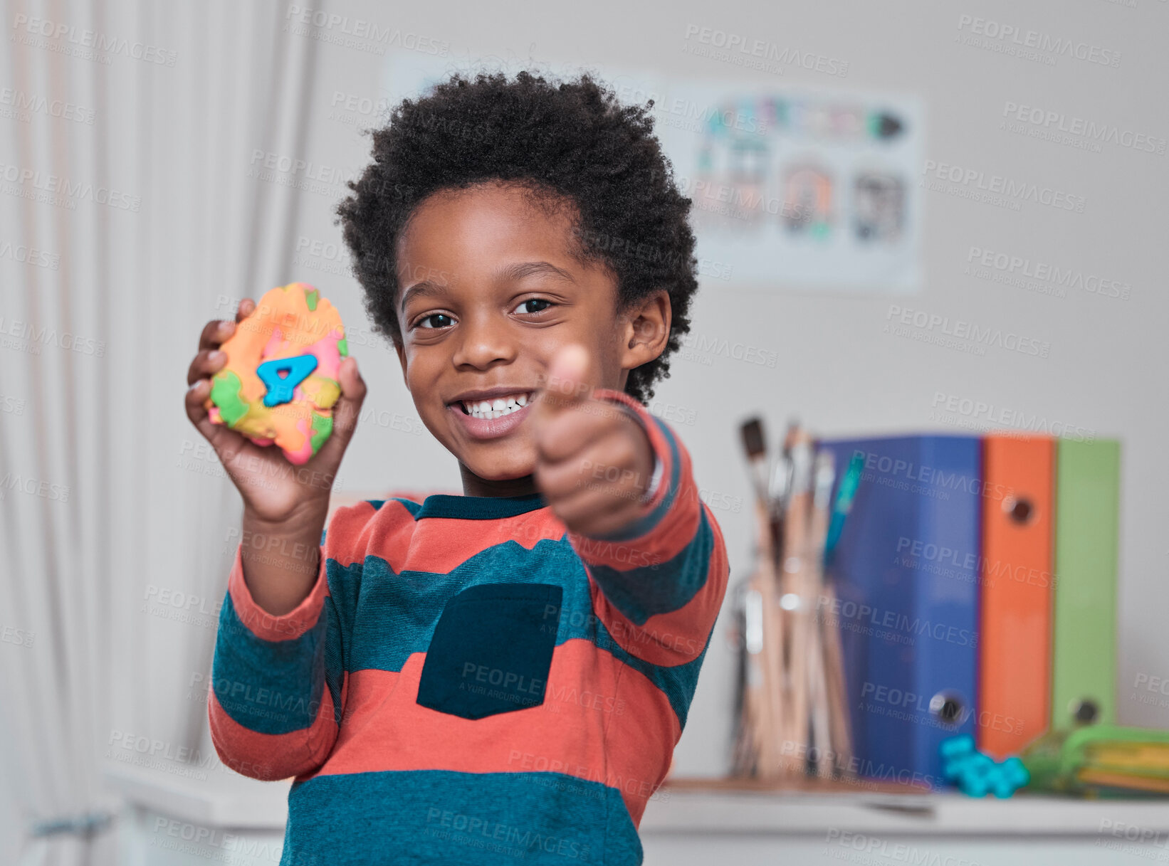 Buy stock photo Shot of a young boy showing thumbs up while holding play dough