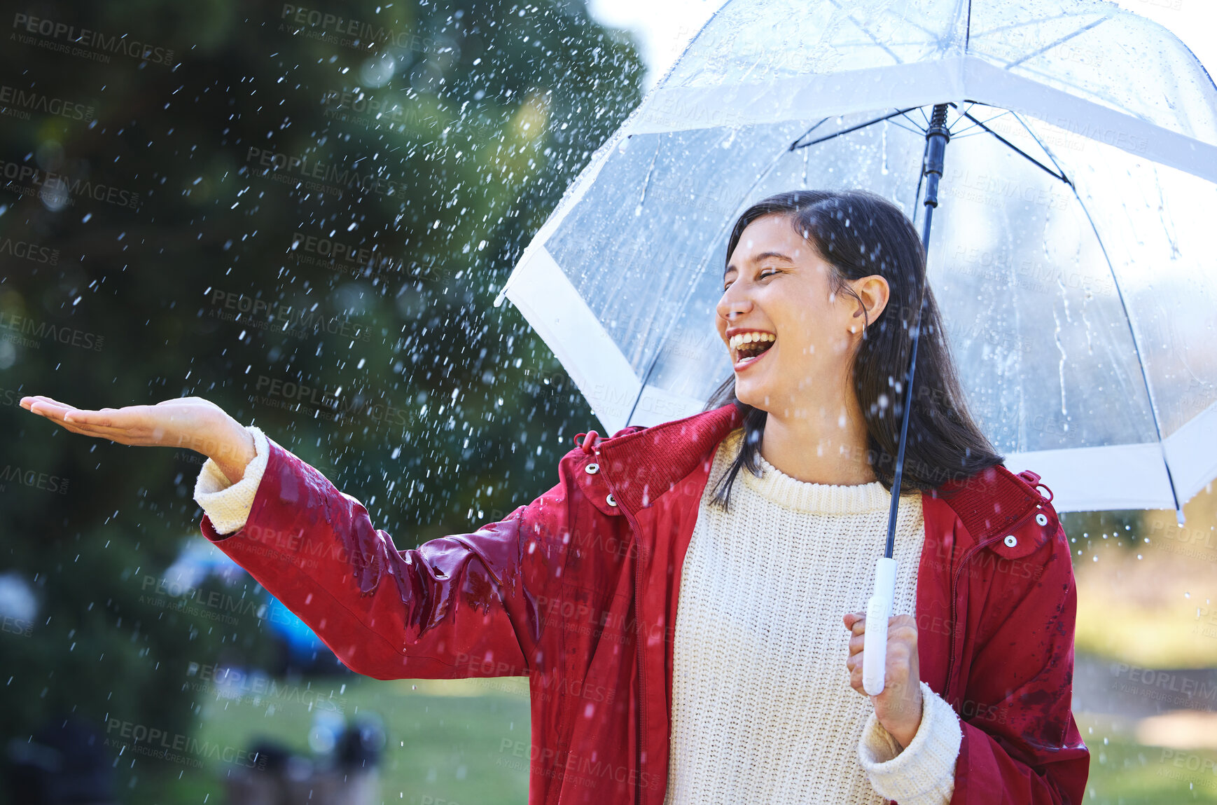 Buy stock photo Shot of a young woman standing in the rain with an umbrella