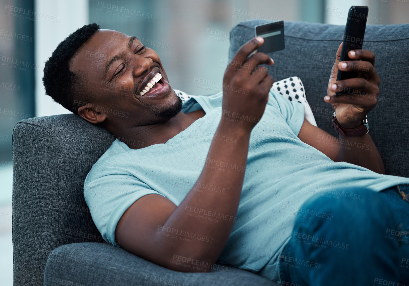 Buy stock photo Shot of a young man using a credit card and phone on the couch at home
