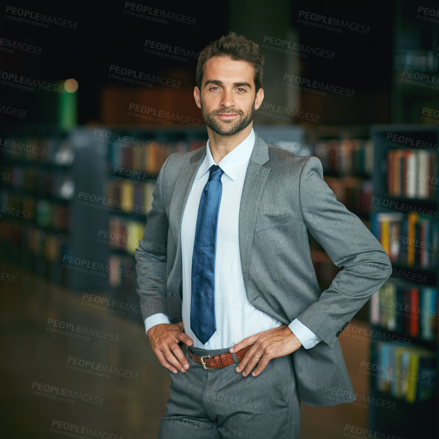 Buy stock photo Cropped portrait of a handsome young businessman standing with his hands on his hips in an empty library