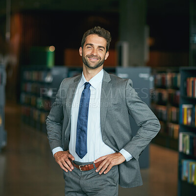 Buy stock photo Cropped portrait of a handsome young businessman standing with his hands on his hips in an empty library