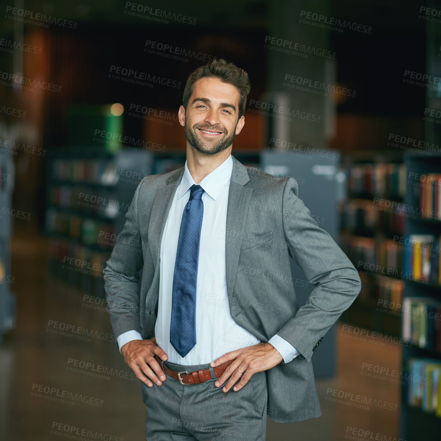 Buy stock photo Cropped portrait of a handsome young businessman standing with his hands on his hips in an empty library