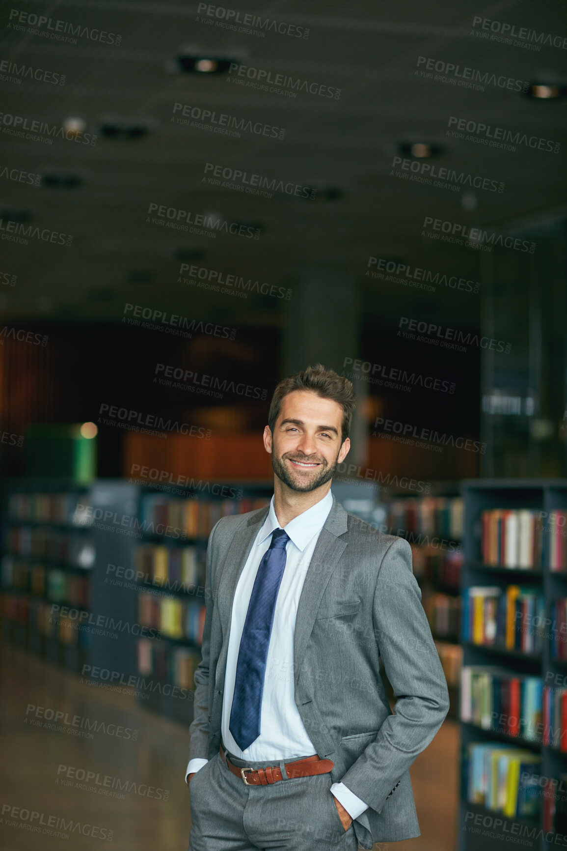 Buy stock photo Cropped portrait of a handsome young businessman standing with his hands in his pockets in an empty library