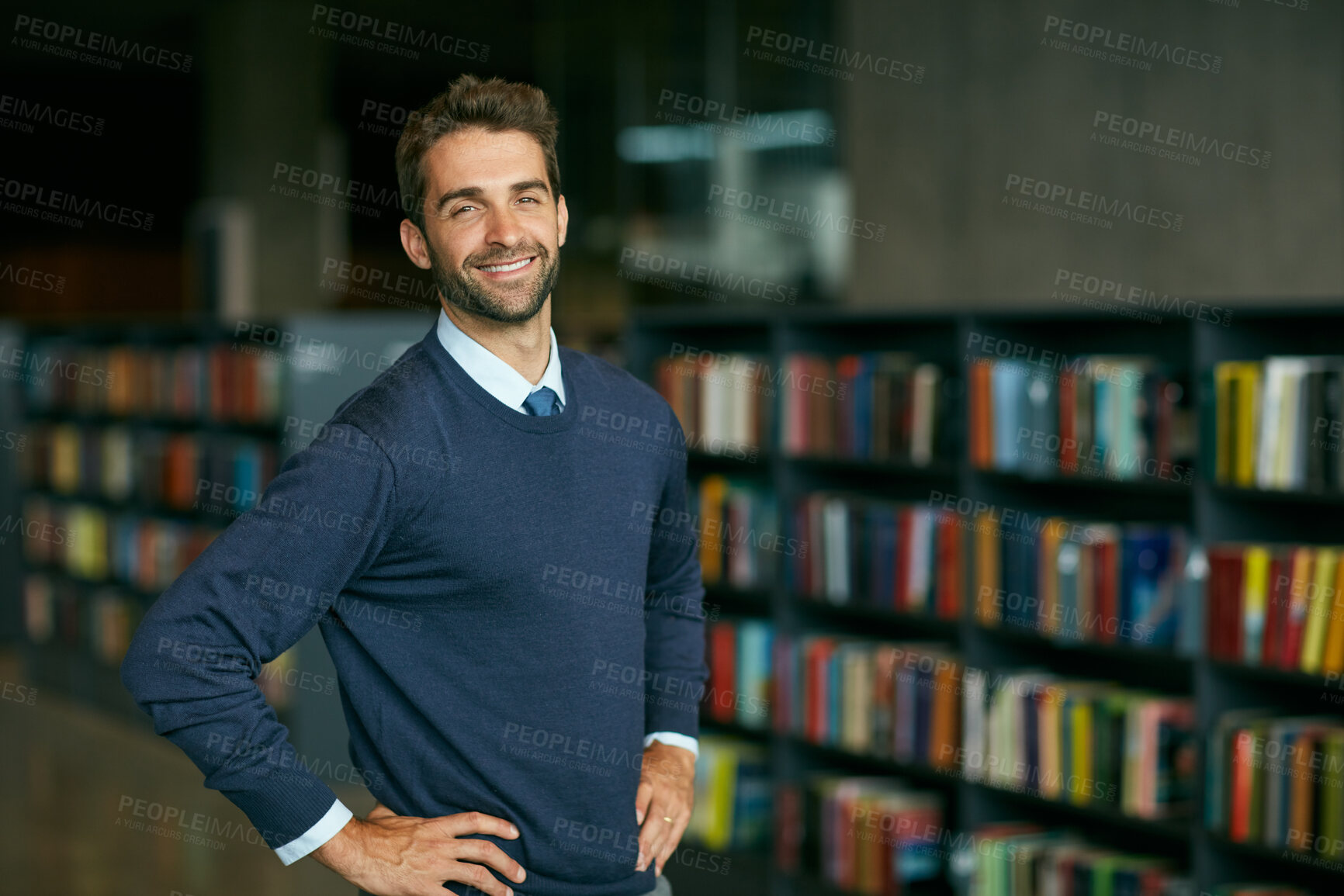 Buy stock photo Cropped portrait of a handsome young businessman standing with his hands on his hips in an empty library