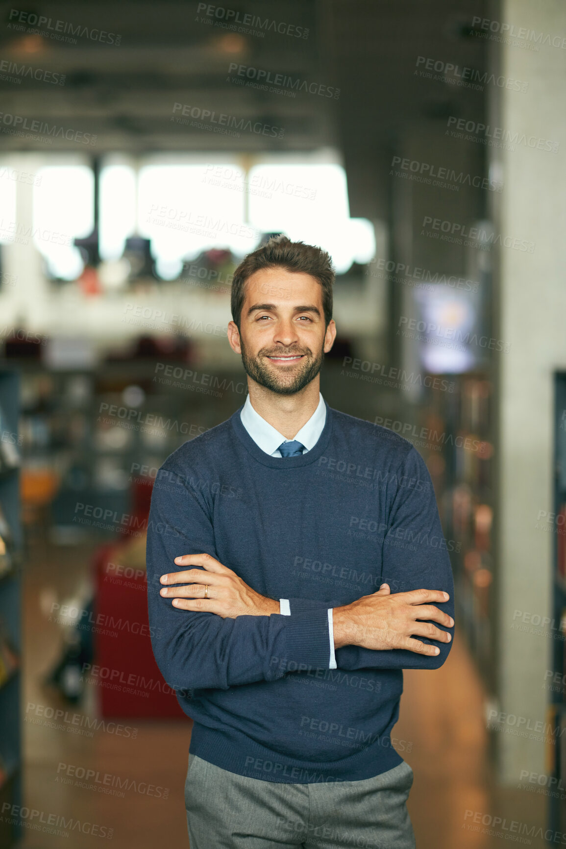 Buy stock photo Cropped portrait of a handsome young businessman standing with his arms crossed in a library