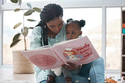 Buy stock photo Shot of a woman reading a book to her daughter while sitting at home