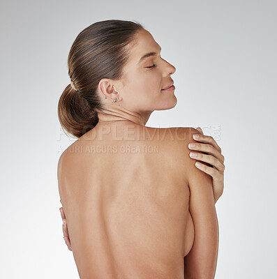 Buy stock photo Rearview studio shot of a young woman embracing her body against a grey background