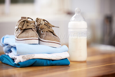 Buy stock photo Home, baby clothes and shoes with milk bottle, prepare for infant and calcium on wooden table. Empty, sneakers and nutrition with fashion for newborn, layout and fresh with folded laundry in house