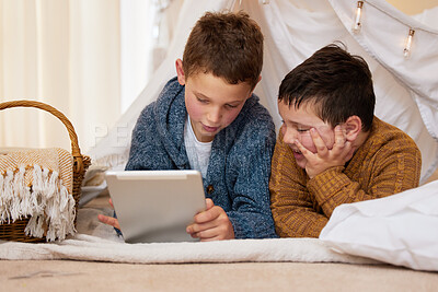 Buy stock photo Shot of two brothers using a digital tablet together under a blanket fort at home
