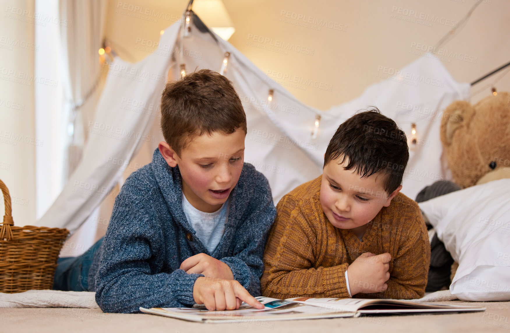 Buy stock photo Shot of two brothers reading a book together under a blanket fort at home
