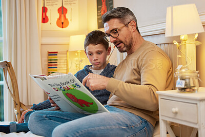 Buy stock photo Shot of a father and son reading a book about dinosaurs together in a bedroom at home