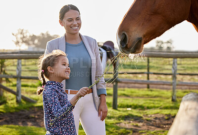 Buy stock photo Shot of an adorable little girl feeding a horse on her farm while her mother looks on