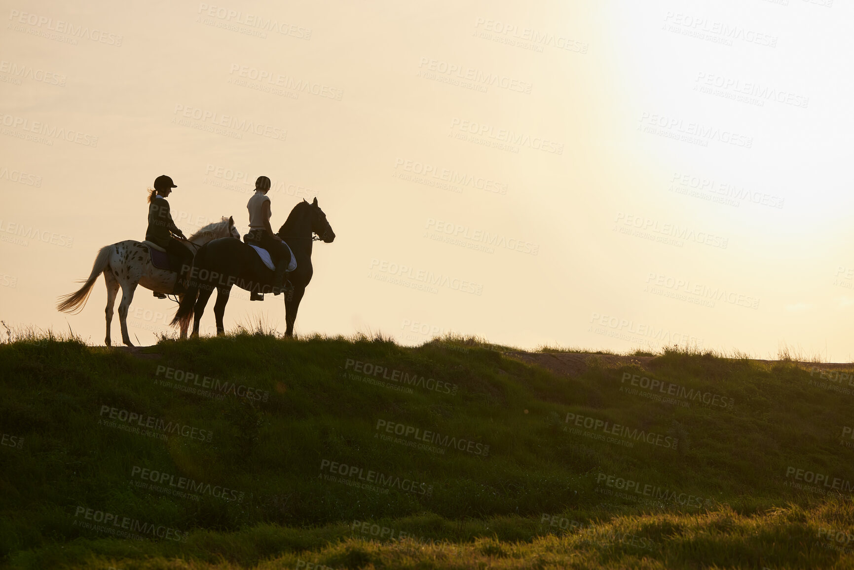 Buy stock photo Shot of two unrecognizable women riding their horses outside on a field
