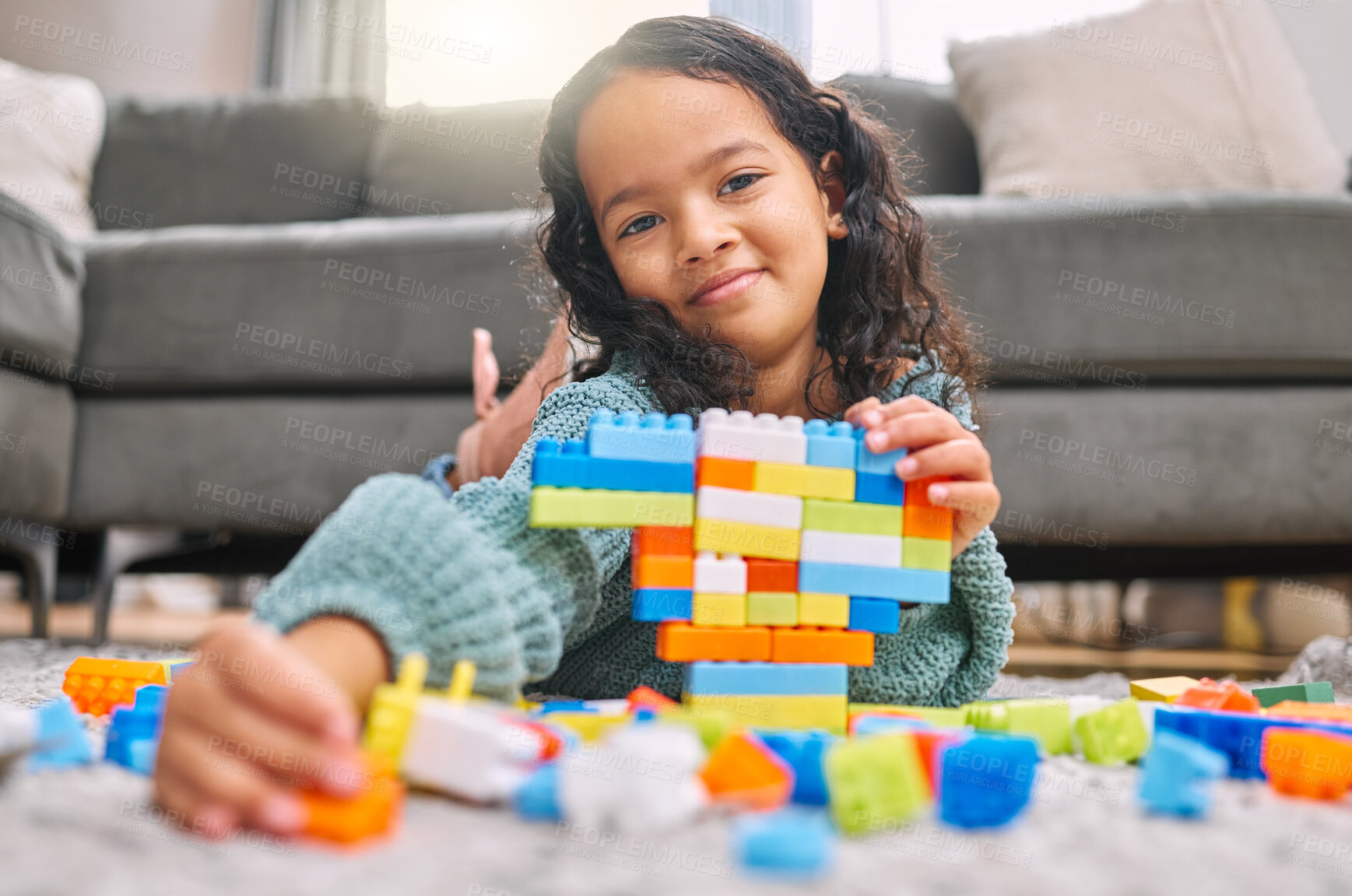 Buy stock photo Shot of an adorable little girl lying on the living room floor at home and playing with builder blocks