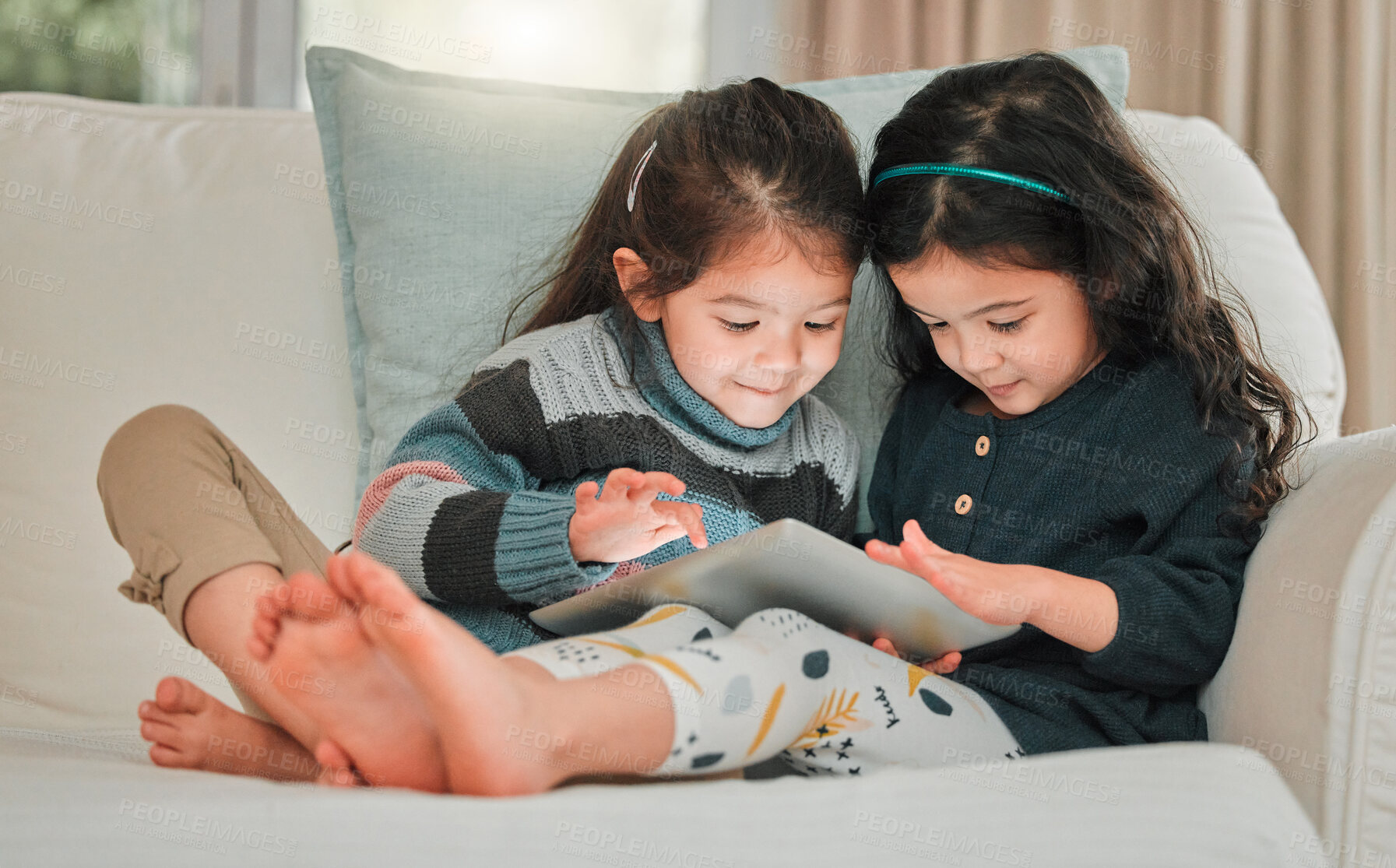 Buy stock photo Shot of two young sisters using a digital tablet together on the sofa at home