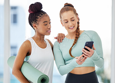 Buy stock photo Shot of two young women standing together and using a cellphone after their yoga practise in the studio