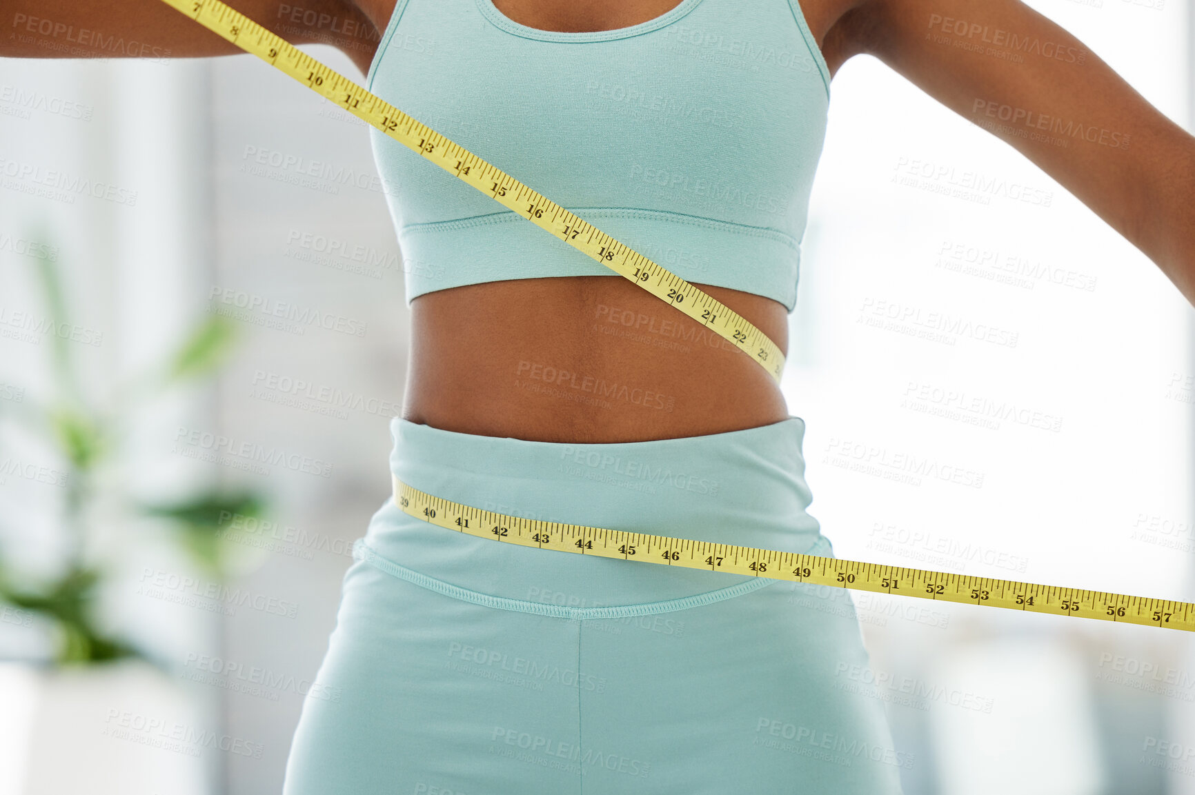 Buy stock photo Cropped shot of an unrecognisable woman standing alone and using a measuring tape around her waist in a yoga studio