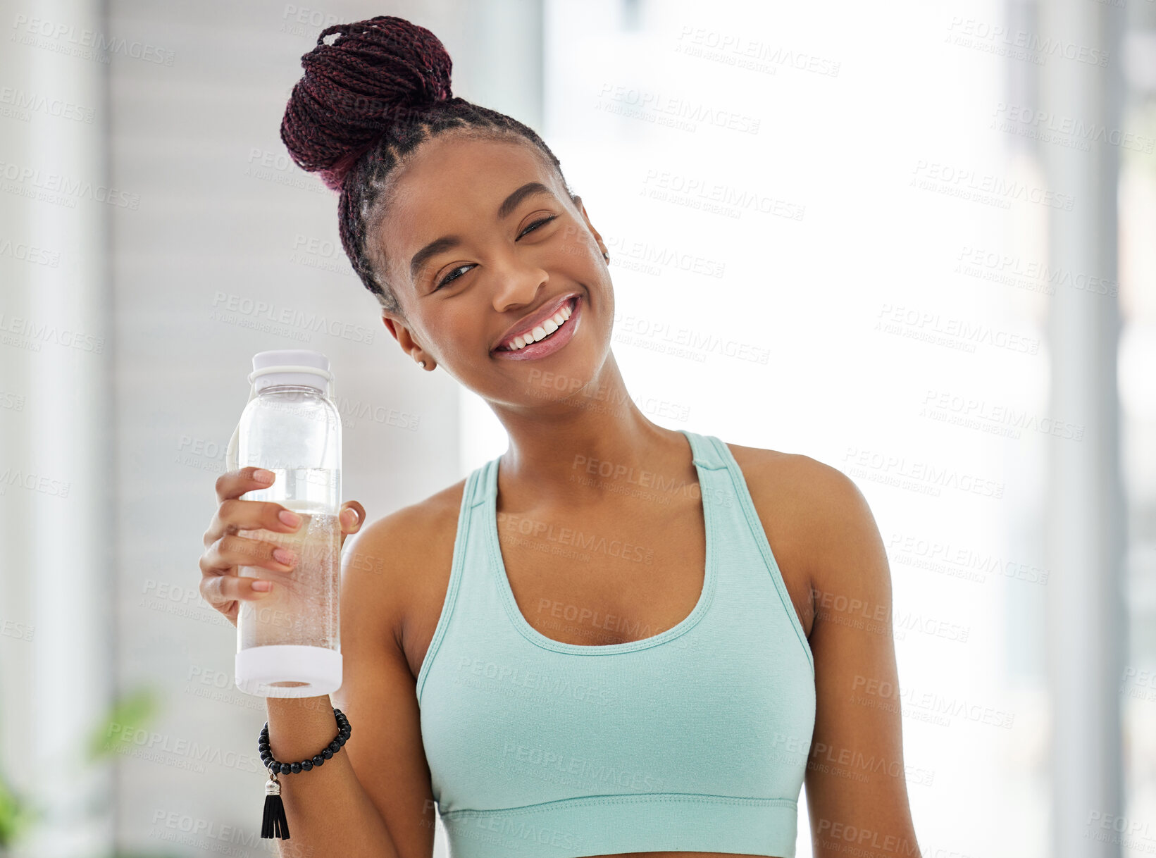 Buy stock photo Shot of an attractive young woman standing alone and holding a bottle of water after practising yoga