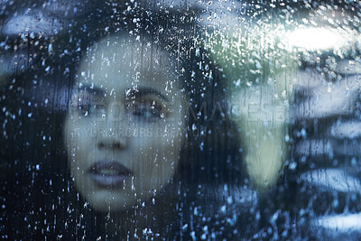 Buy stock photo Shot of a young woman looking thoughtfully out a window on a rainy day