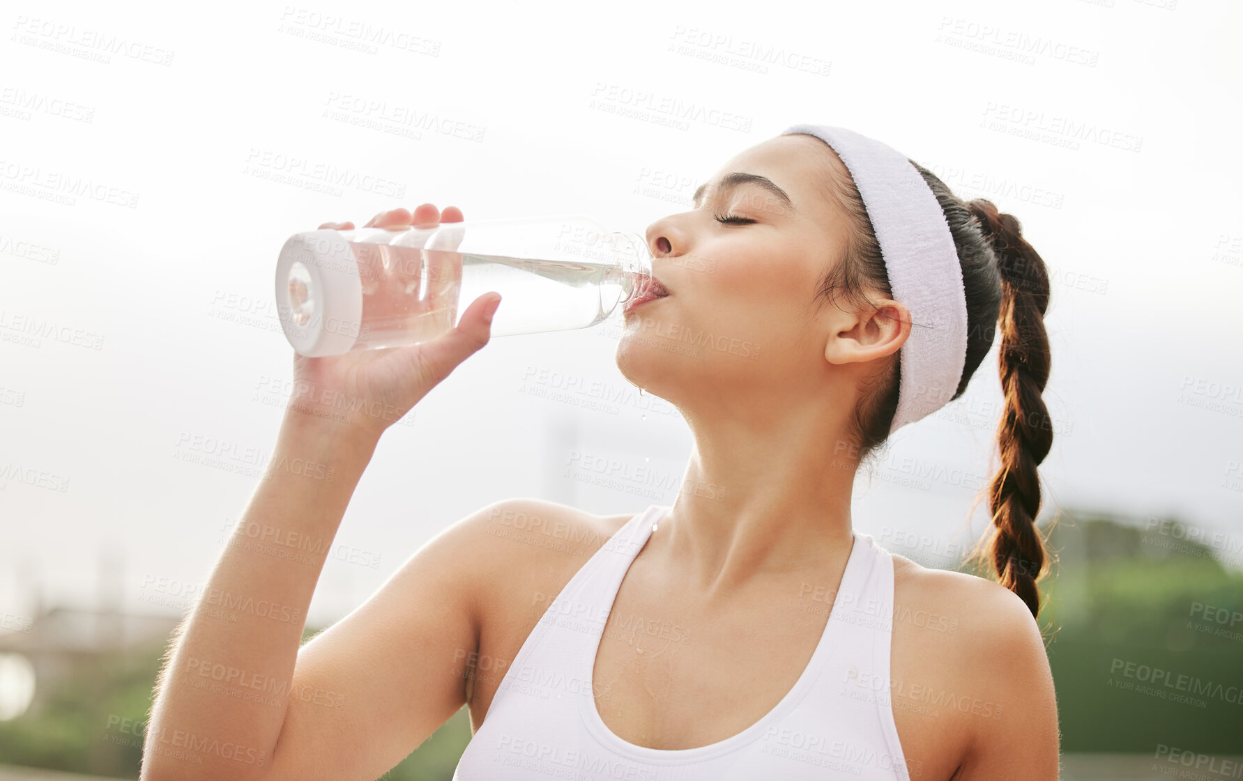 Buy stock photo Shot of a beautiful young woman drinking a bottle of water while out playing tennis