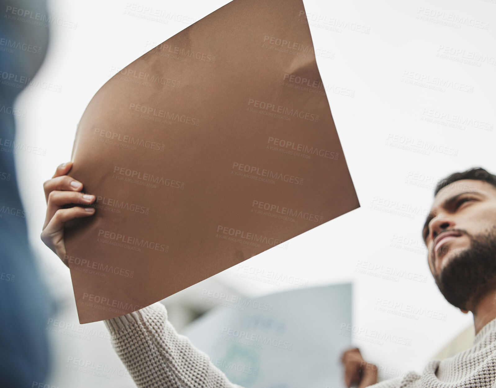 Buy stock photo Low angle shot of a handsome young man holding a sign while taking part in a political rally