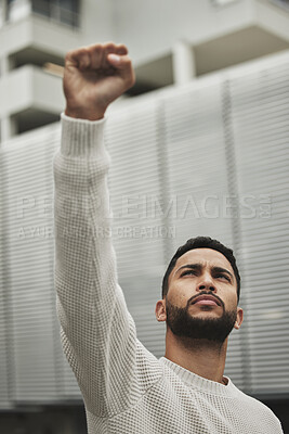 Buy stock photo Low angle shot of a handsome young man raising his fist in protest while fighting for his rights